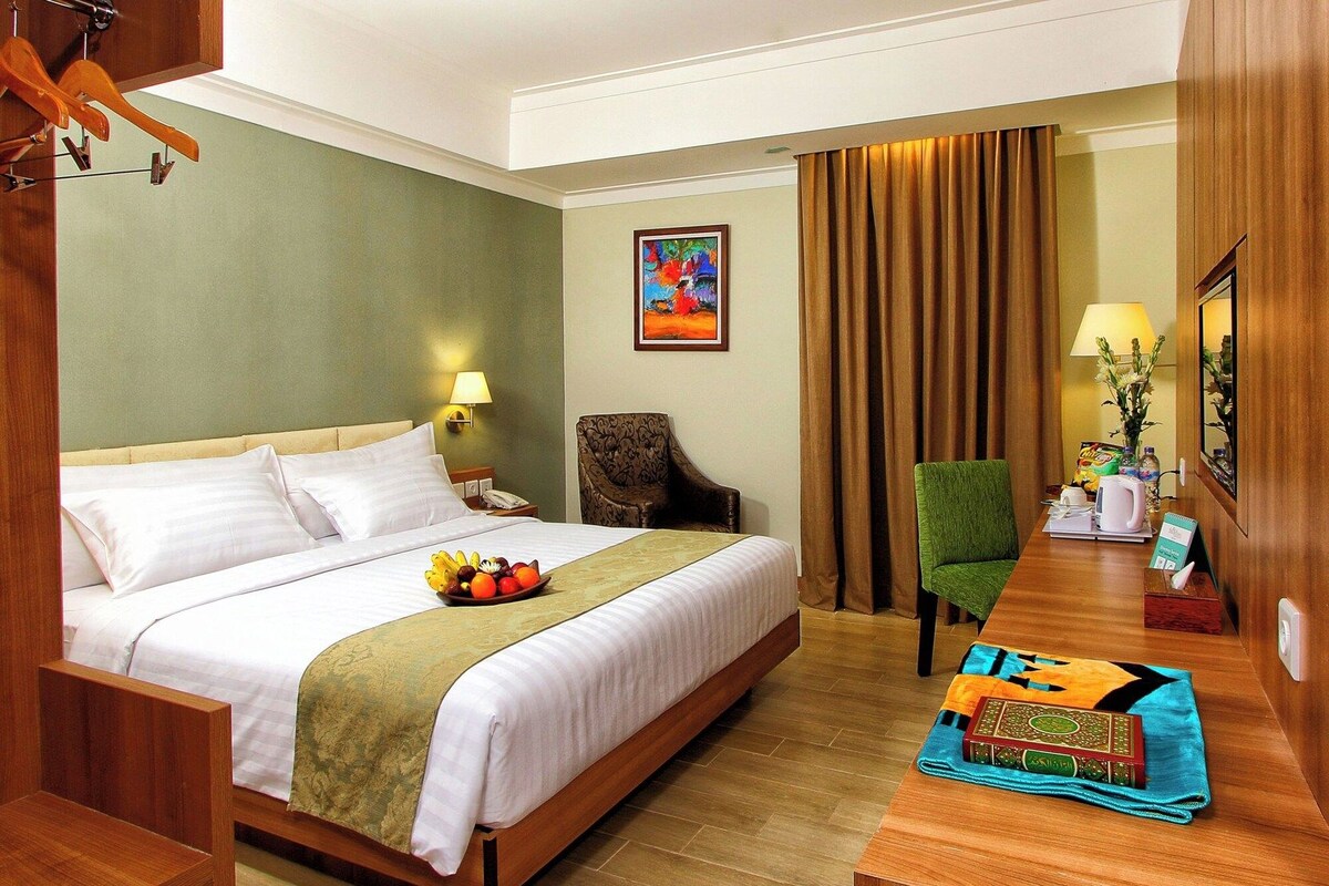 A hotel room with a bed, a desk, a chair, a lamp, and a painting on the wall.