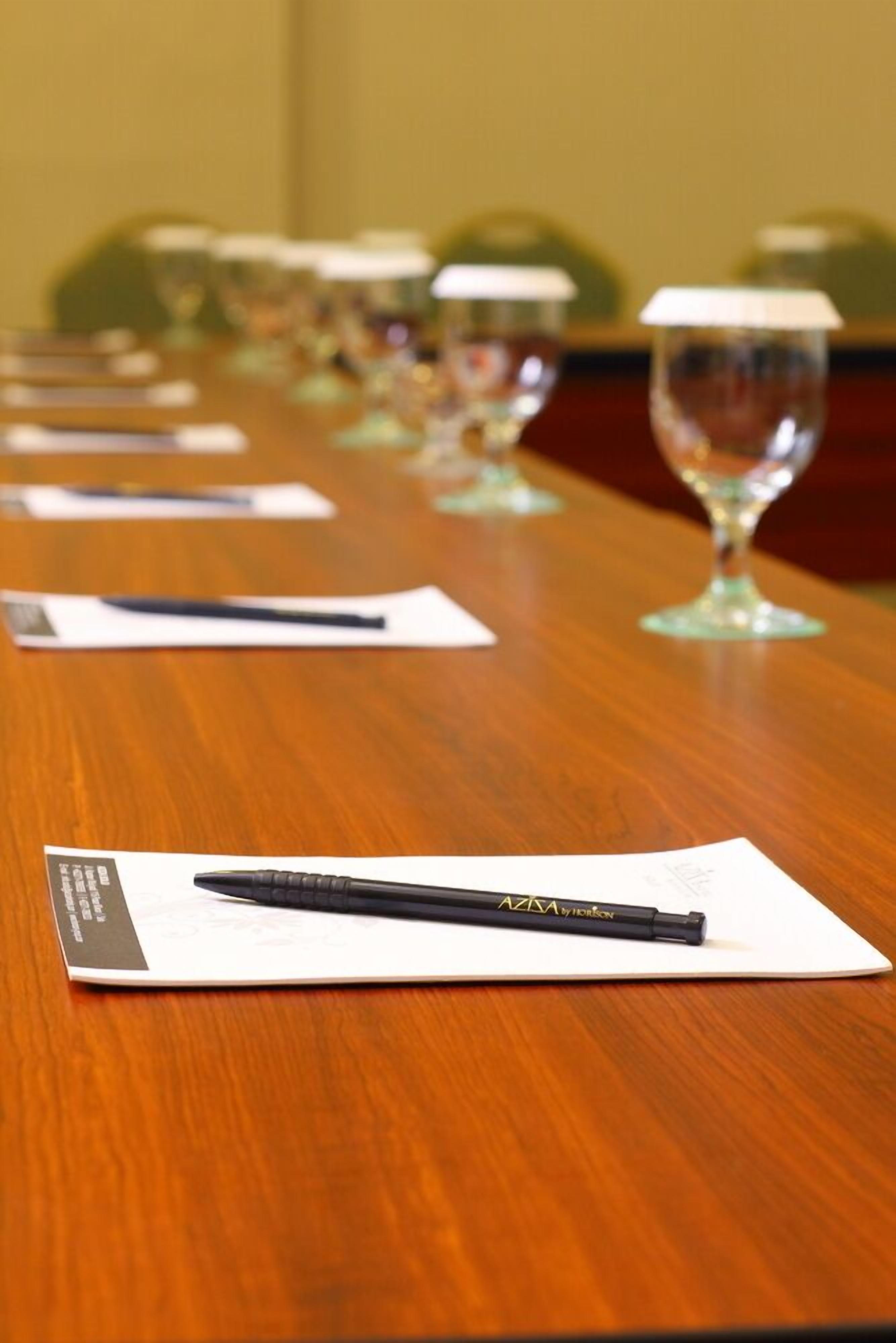 Een vergaderruimte met een tafel, een pen, papieren, brillen en een stoel op de achtergrond.