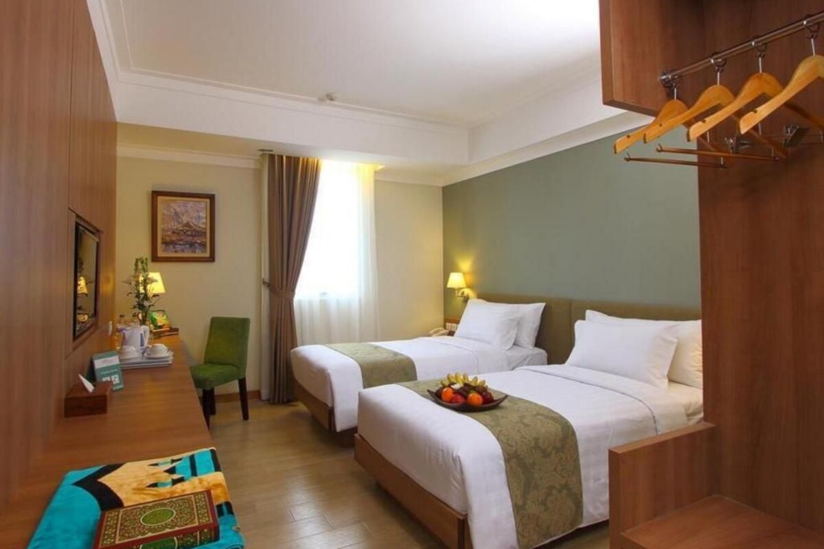 A hotel room with two beds, a desk, a chair, a small table, and a hanging coat rack.