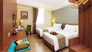 A hotel room with two beds, a desk with a lamp, a chair, a wooden coat rack, and a framed picture on the wall.