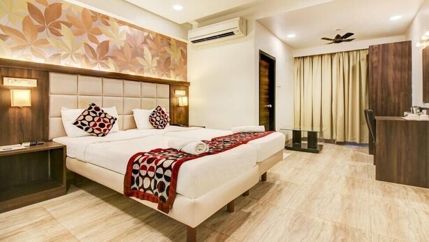 A hotel room with a large bed, a desk, a chair, an air conditioner, and a ceiling fan. - Krishna Avatar Stay Inn (Navi Mumbai)