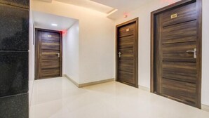 A hallway with three dark wooden doors, each marked with a number. The floor is tiled, and the walls are light-colored. - Krishna Avatar Stay Inn (Navi Mumbai)