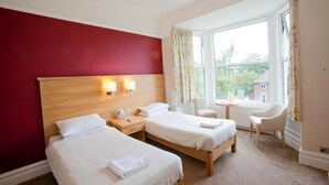 A hotel room with two beds, a wooden headboard, a small table, a chair, and a window with curtains.
