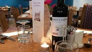 A dining table set with cutlery, a bottle of Footsteps wine, a candle, and a menu.