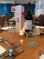 A dining table set with cutlery, a bottle of Footsteps wine, a candle, and a menu.