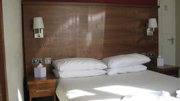 A hotel room with a wooden headboard, two bedside tables with lamps, a bed with white linens, and a door with a no-smoking sign.