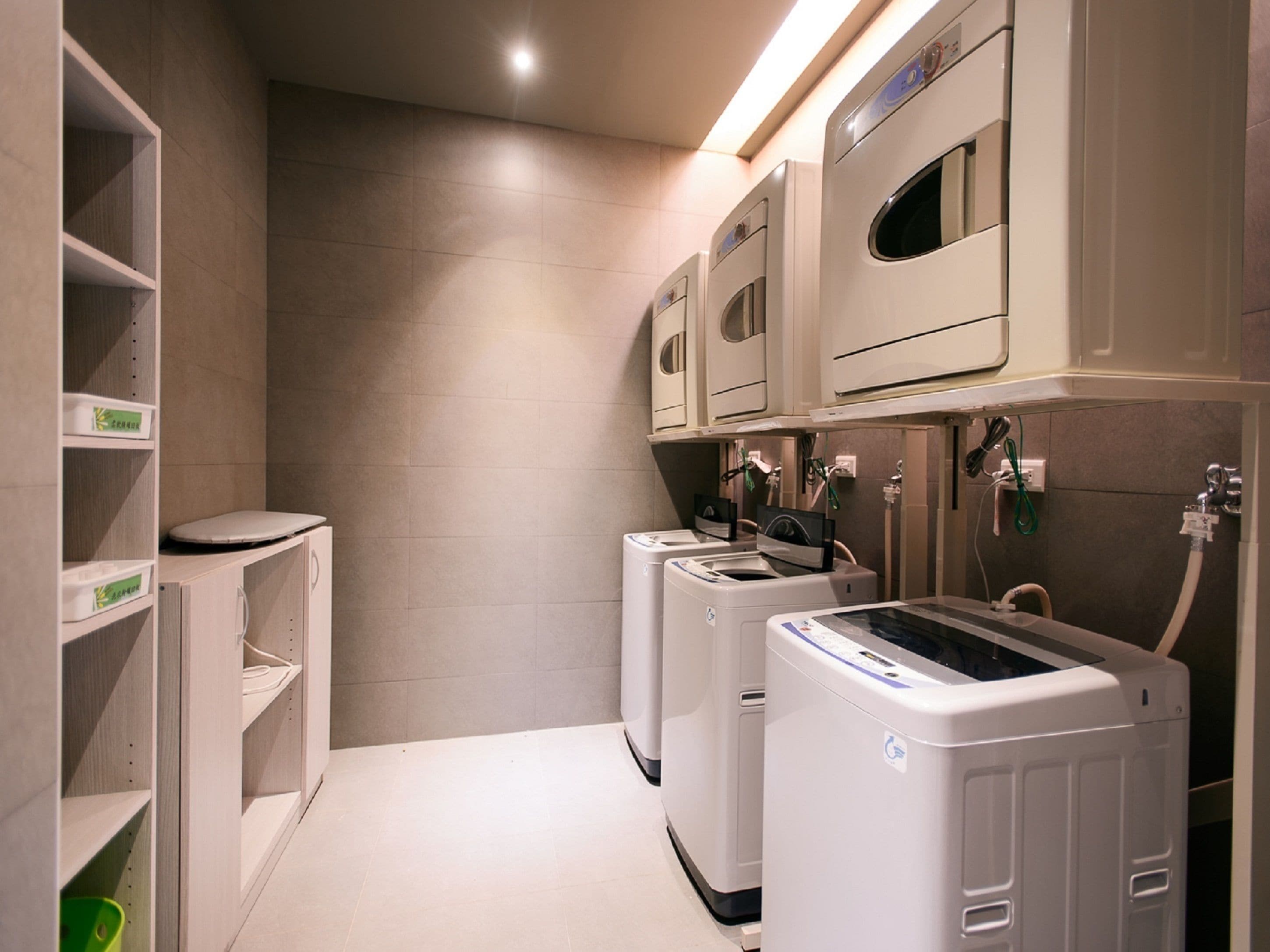 A laundry room with two front-loading washing machines, a shelf with folded towels, and a toilet.