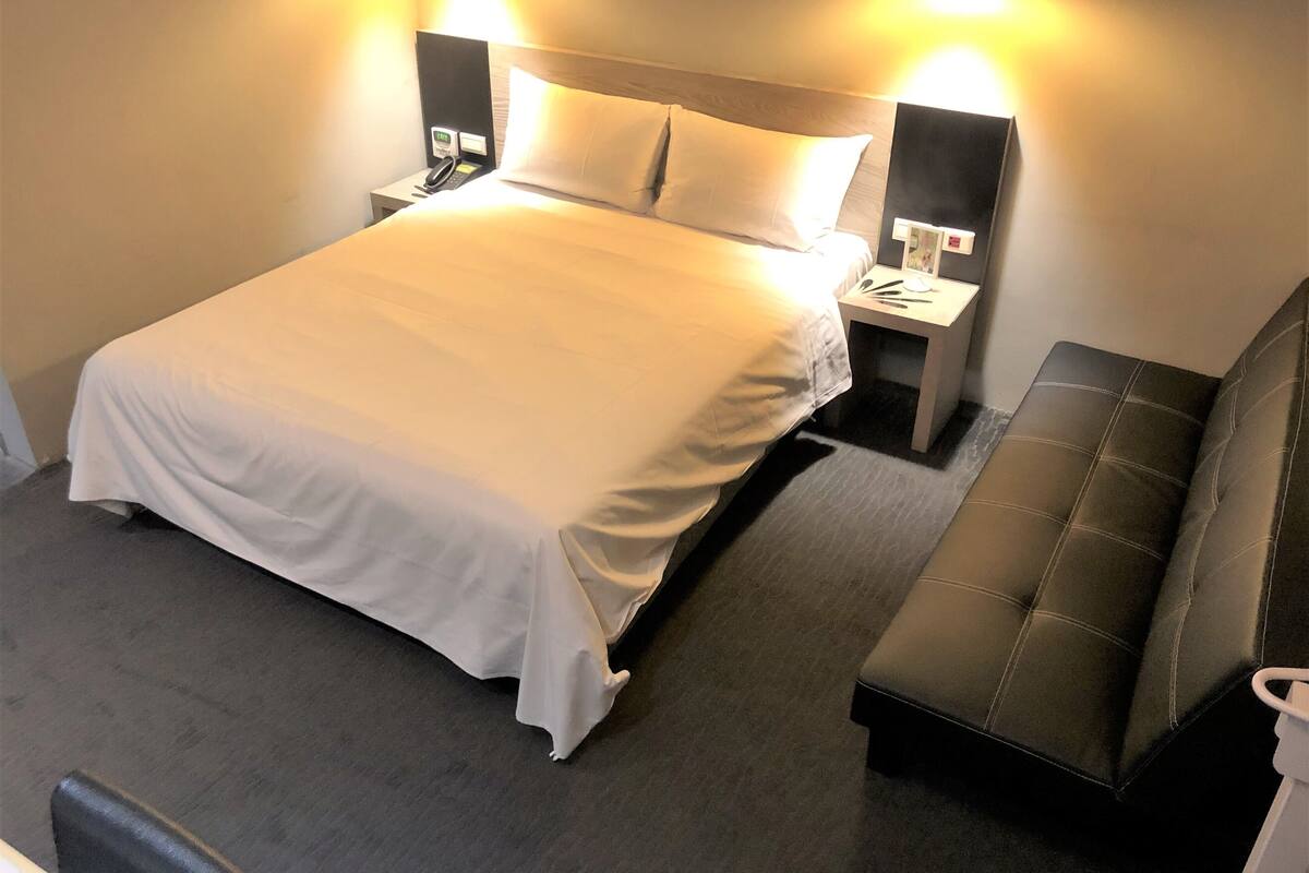 Ein ordentlich bezogenes Bett mit weißer Bettdecke, zwei Nachttische mit Lampen und eine Bank.
