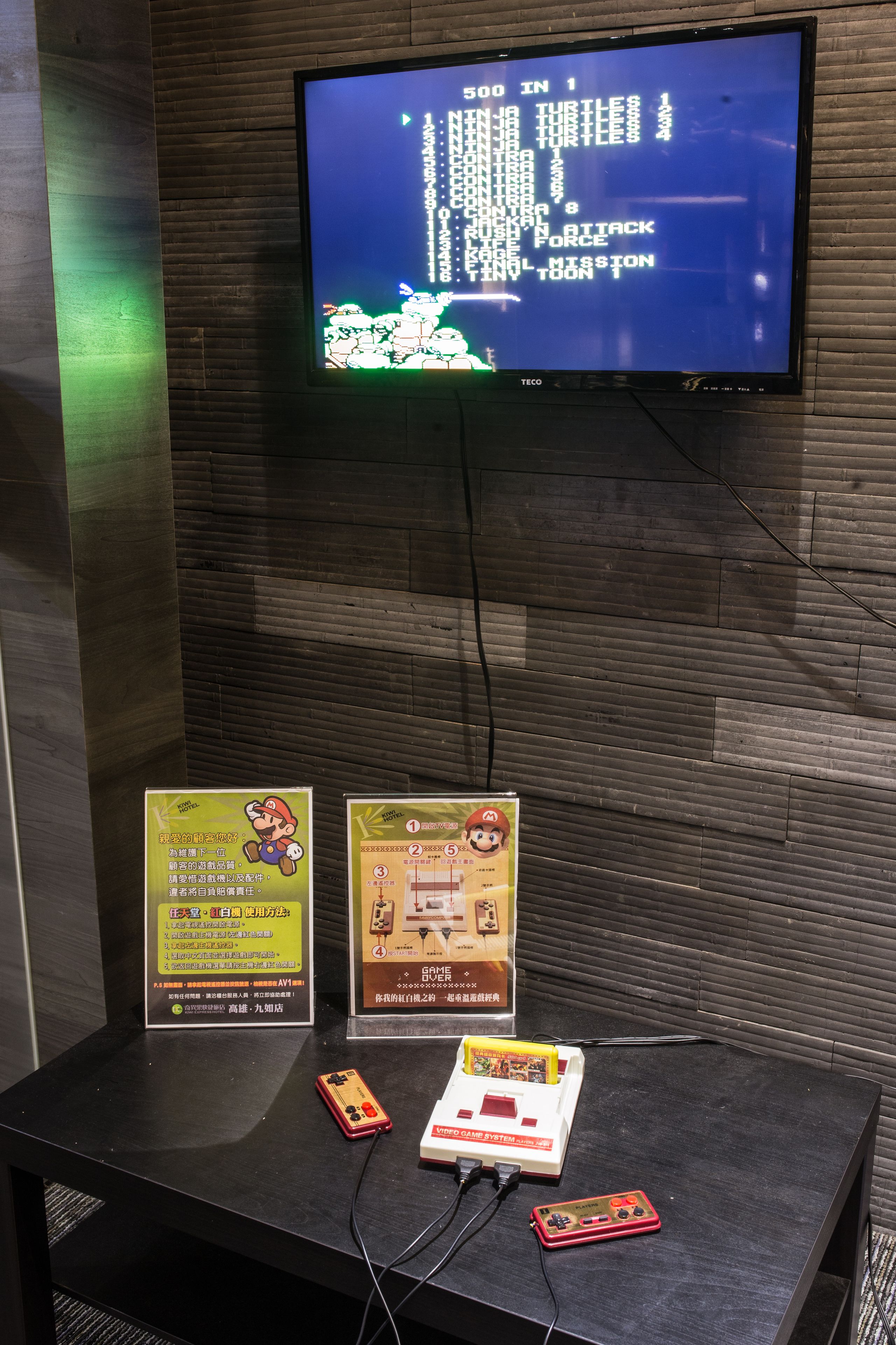 Una habitación con una televisión mostrando un videojuego, una mesa con material promocional y una consola Nintendo Game System.