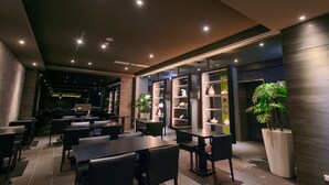 A modern restaurant interior with tables and chairs, recessed lighting, and decorative shelves. - Kiwi Express Hotel - Jiuru (Kaohsiung)