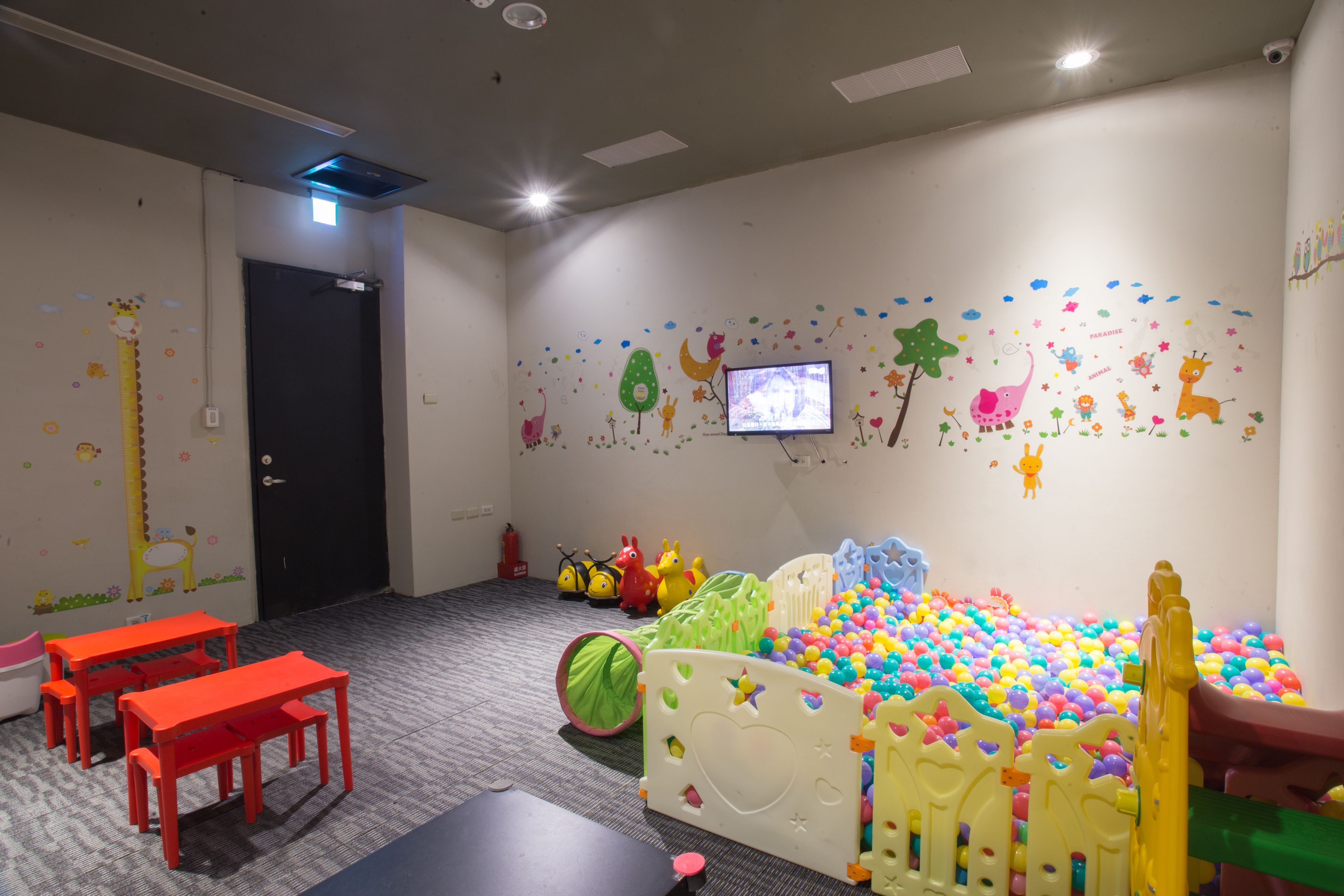 A children's play area with a ball pit, colorful wall decorations, and a television mounted on the wall.