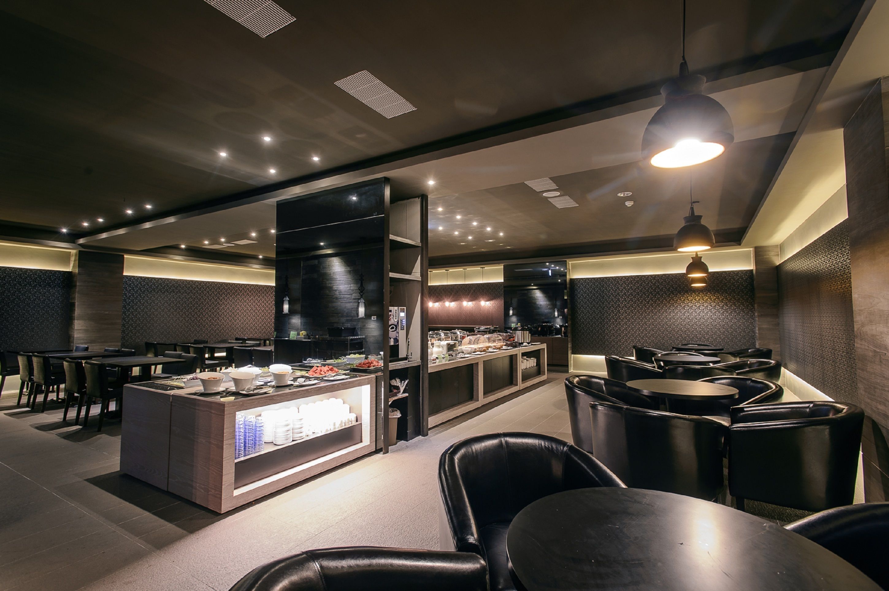 A modern restaurant with a central counter, black leather seating, and recessed lighting.