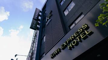 Exterior del Hotel Kiwi Express, con un diseño moderno, destacando un letrero llamativo y un cielo despejado al fondo.