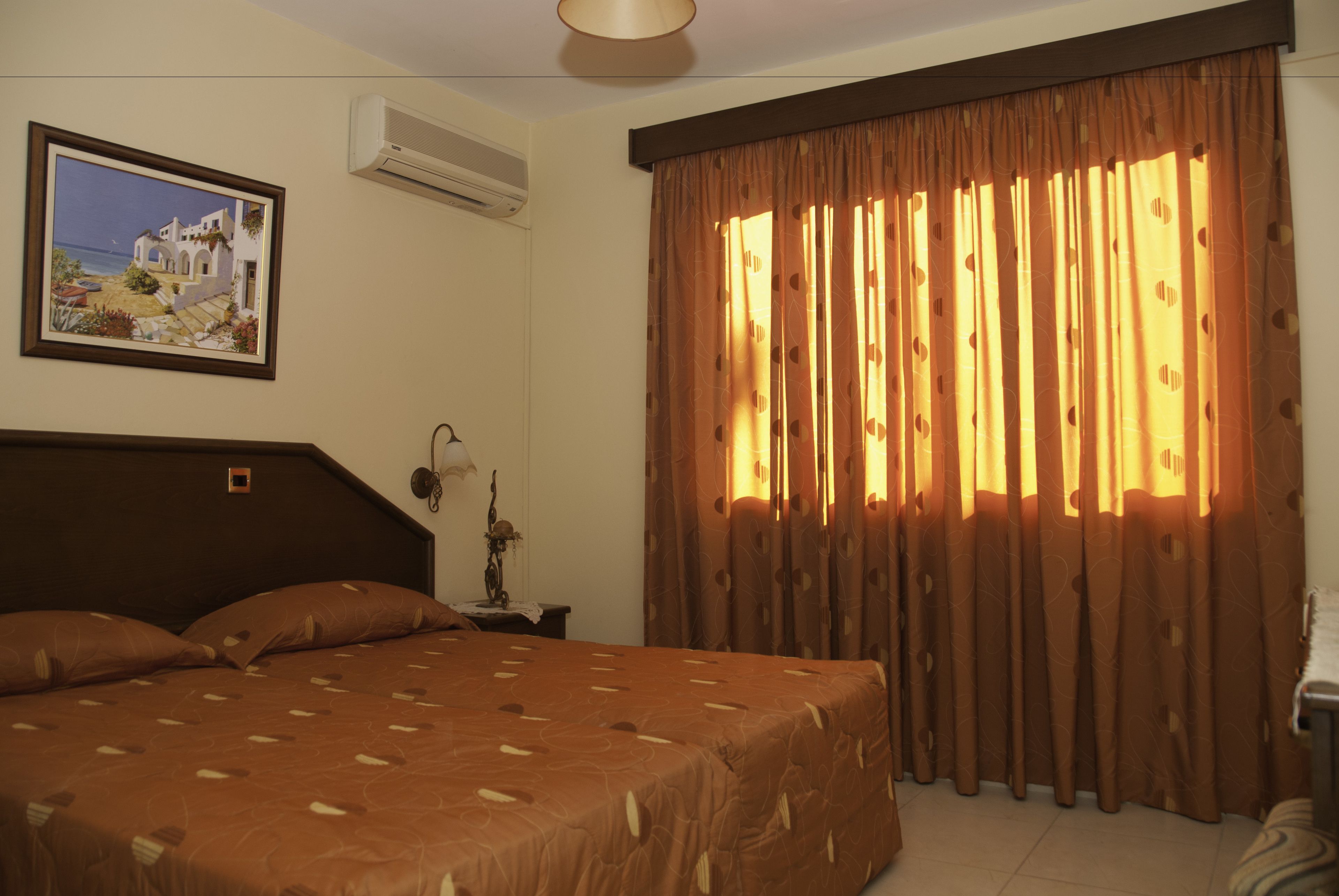 Una habitación de hotel con una cama, una mesita de noche, una lámpara, un cuadro en la pared y cortinas.