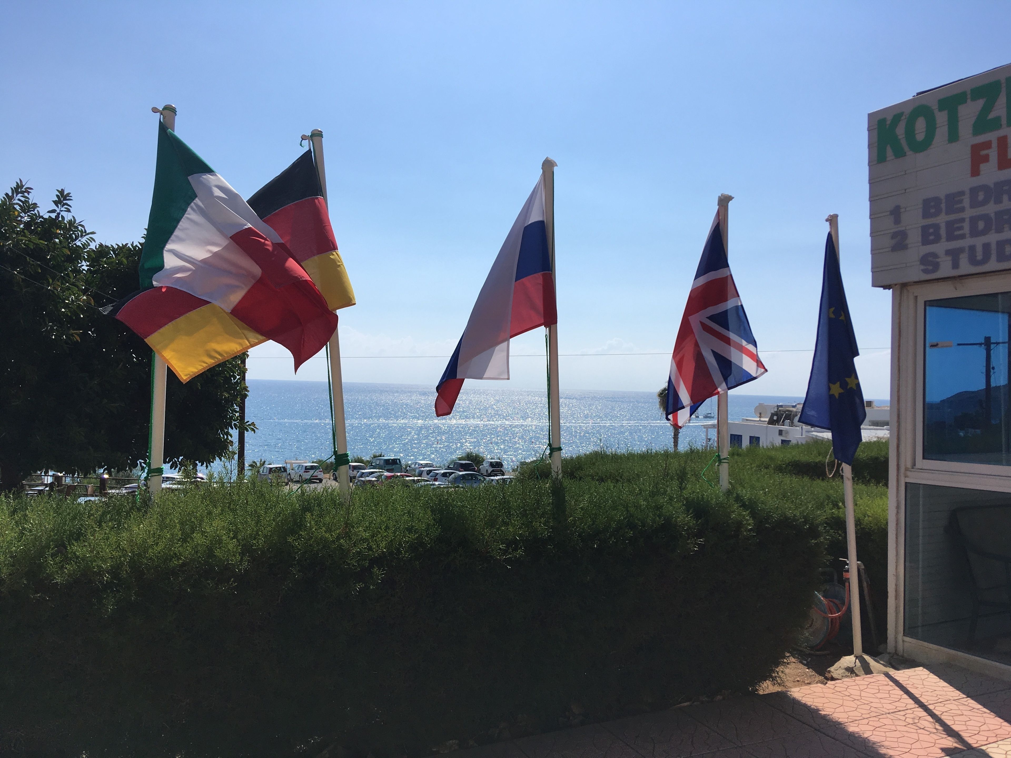Ein Hotelschild mit Flaggen, Meerblick und parkenden Autos.