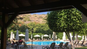 Un espace aménagé au bord de la piscine, avec des chaises longues et des parasols, une terrasse carrelée et une vue sur un paysage vallonné.