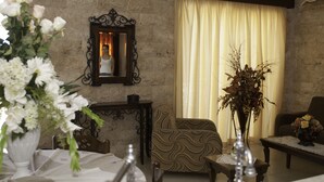 Un salon avec un canapé, une table, un vase de fleurs, un miroir et une fenêtre avec des rideaux.