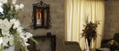 A living room with a sofa, a table, a vase with flowers, a mirror, and a window with curtains.