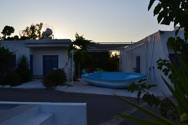 A residential area with a blue boat, a white building with blue shutters, and a clear sky. - Flokkas Hotel Apartments (Paralimni)