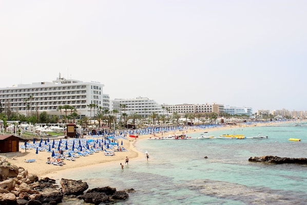A beach resort with multiple hotel buildings, sun loungers, and boats.