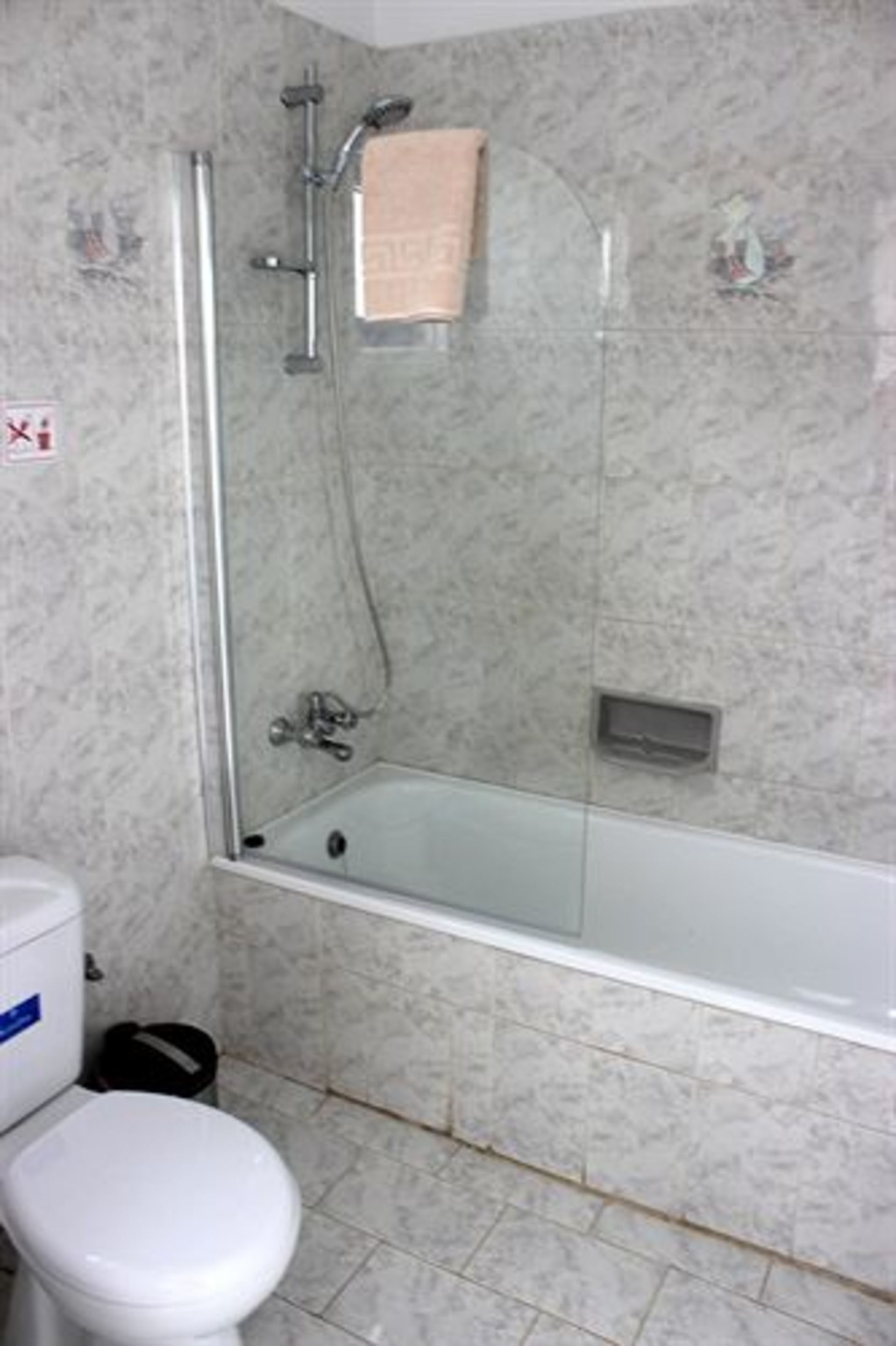Une salle de bain avec une douche à parois de verre, des toilettes blanches et un mur en marbre.