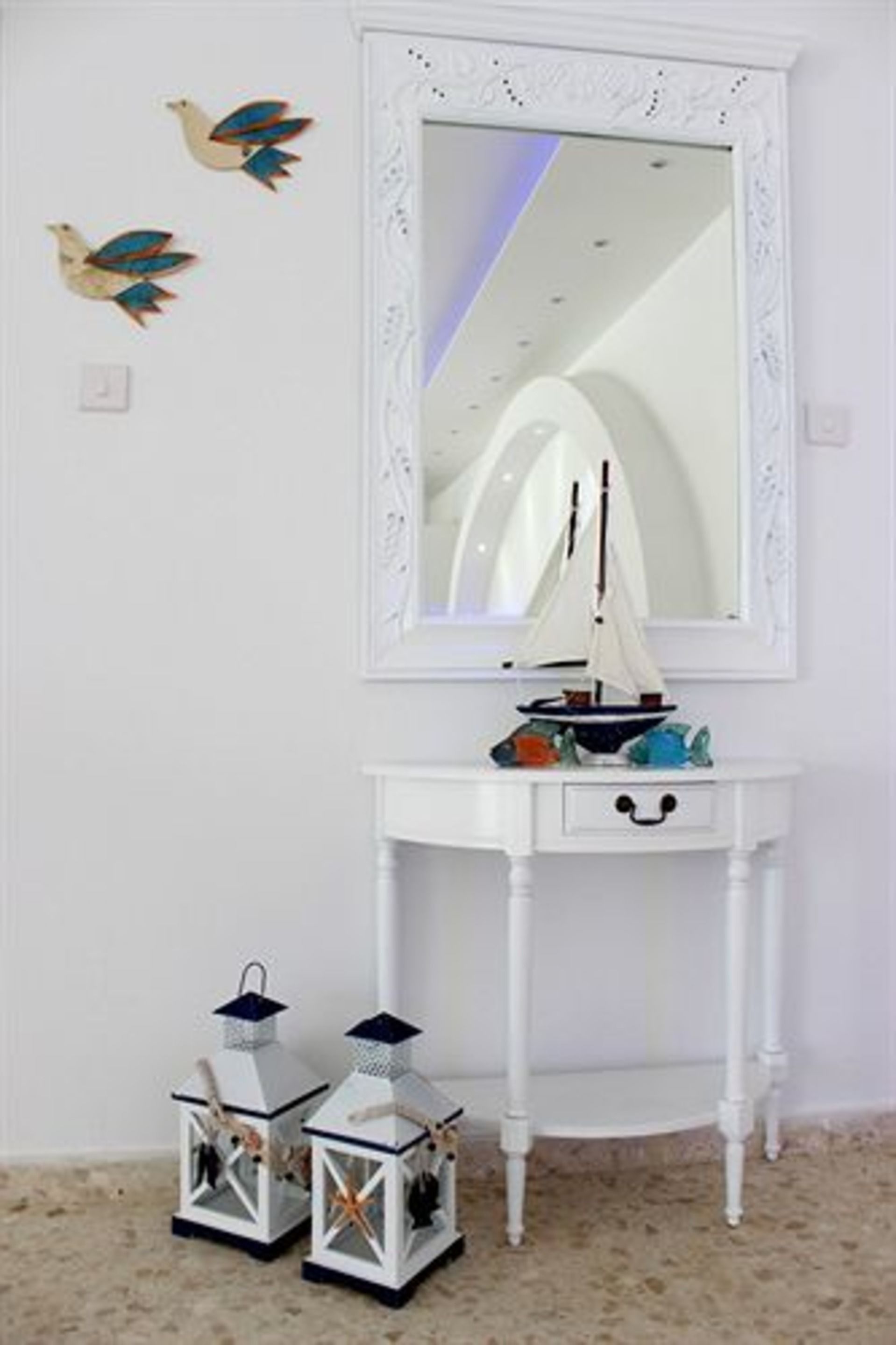 Ein weißes Schminktischchen mit Spiegel, ein kleines Modell eines Segelbootes und zwei dekorative Laternen auf dem Boden.