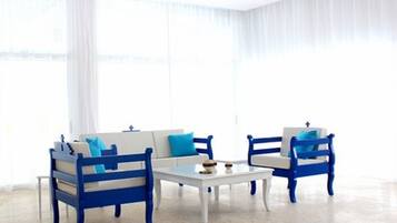 A room with a white sofa and two blue armchairs, a small white table, and sheer white curtains.