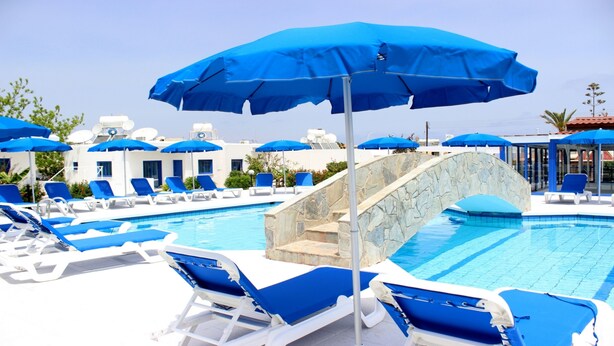Área de piscina com guarda-sóis azuis, cadeiras de descanso brancas e uma ponte de pedra.