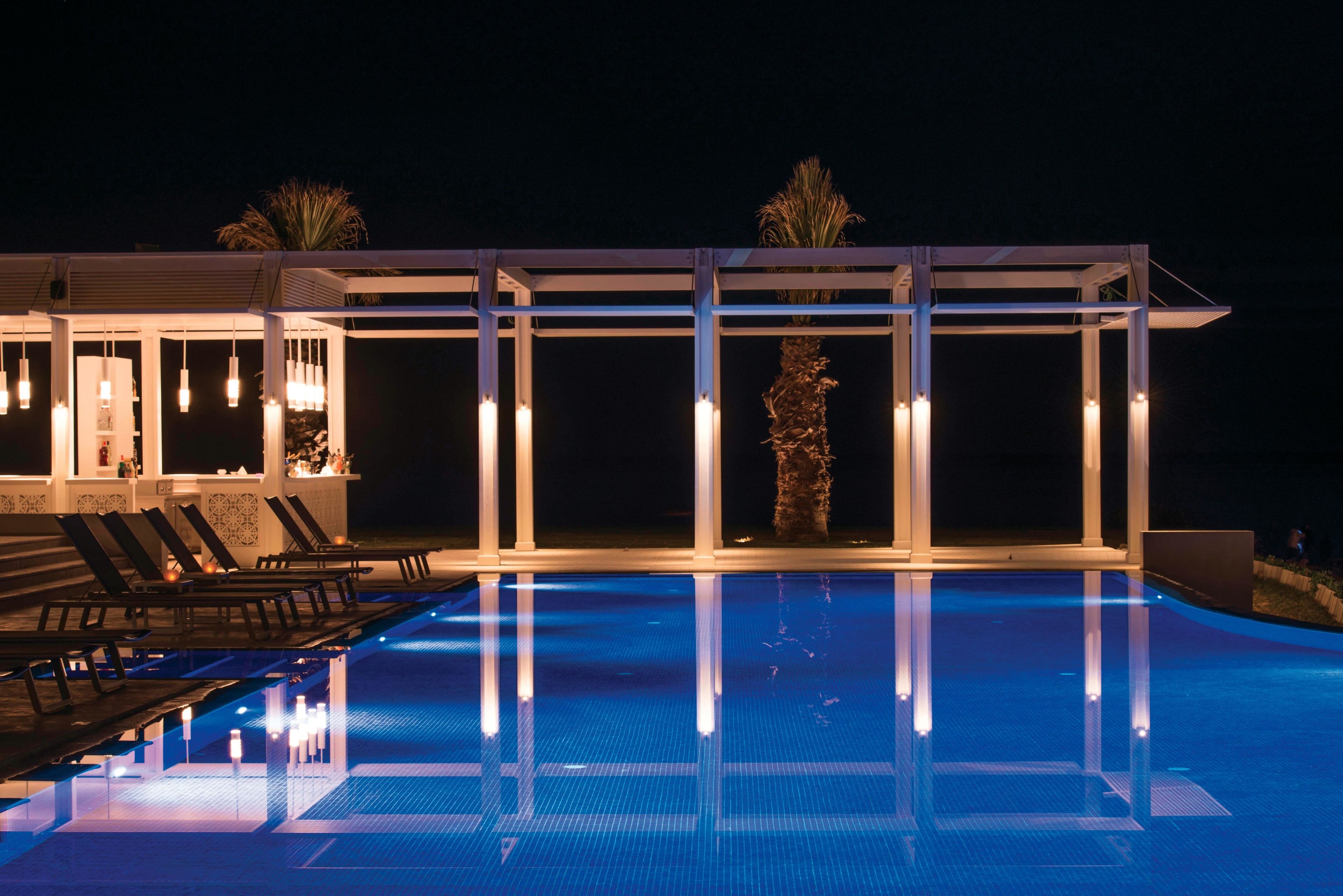 A swimming pool with a glass enclosure, lounge chairs, and a palm tree.