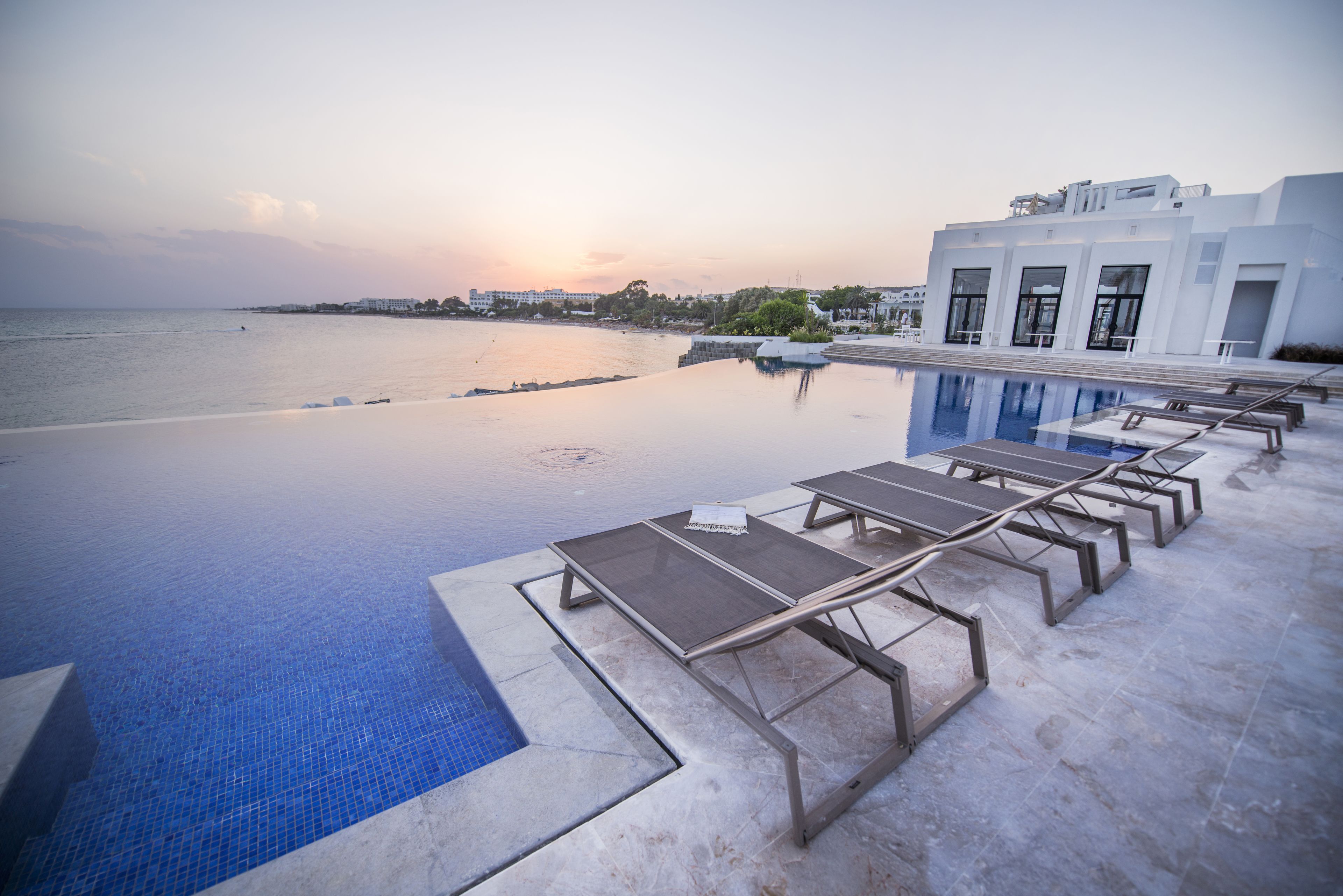 Una piscina infinita con vistas al mar y un edificio moderno al fondo.