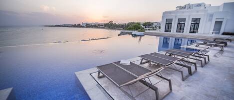 Una piscina infinita con vistas al mar y un edificio moderno al fondo.