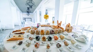 A breakfast buffet with various food items and utensils arranged on a round table in a bright, spacious room with large windows. - La Badira - Adults Only (Hammamet)