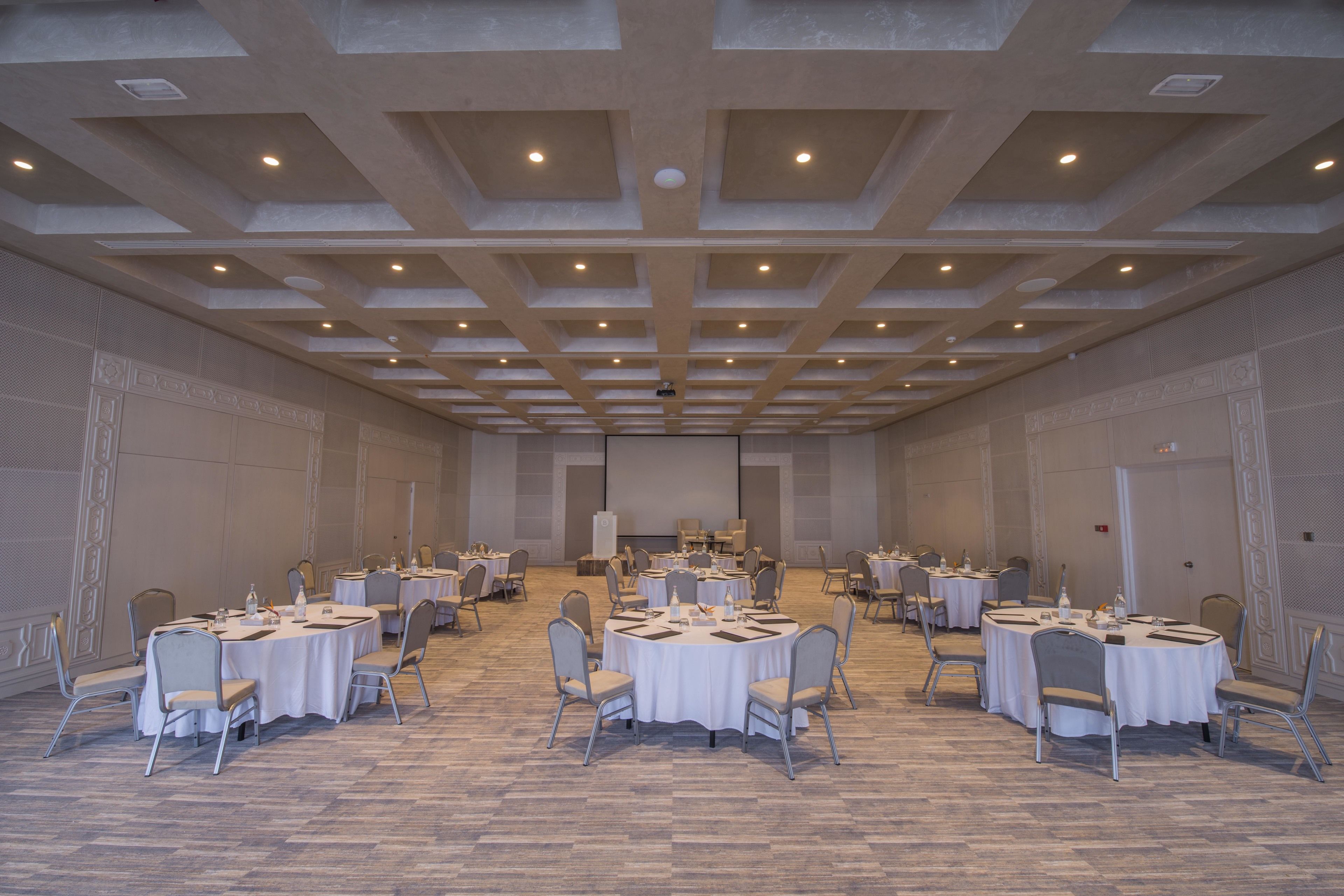 A large conference room with multiple round tables and chairs, arranged in a symmetrical layout.