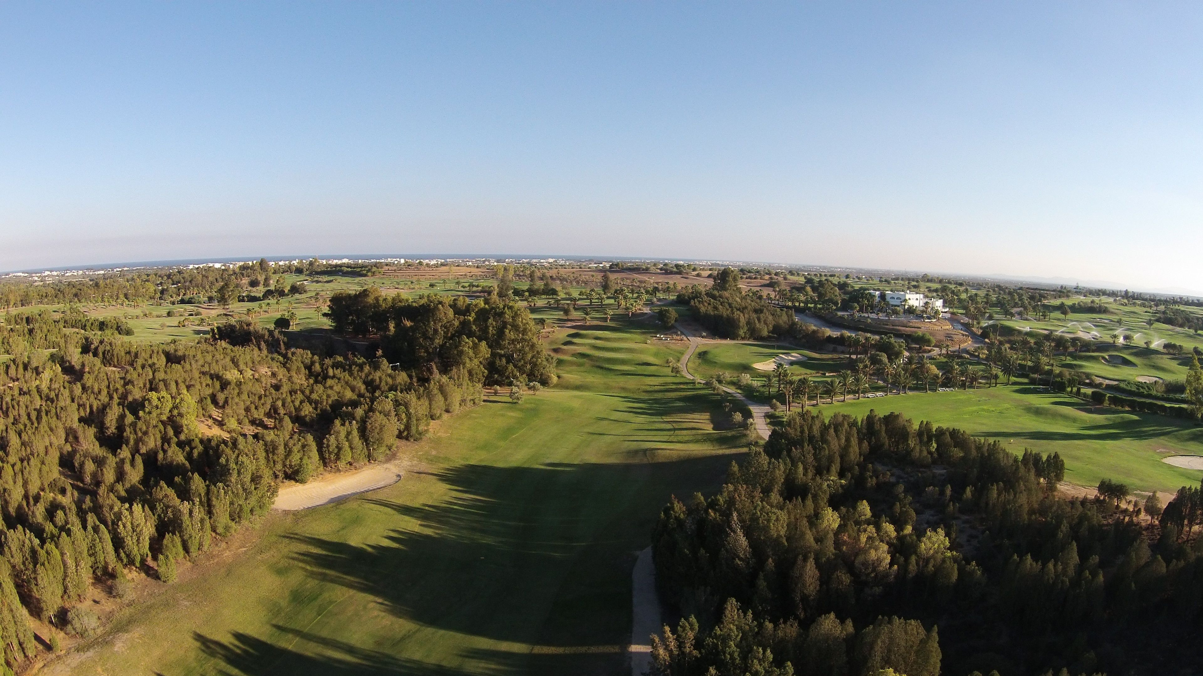 A golf course with a clubhouse, surrounded by dense forests and open fields.