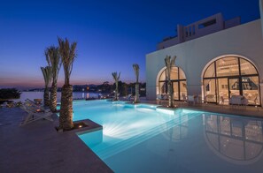 A modern pool area with lounge chairs and palm trees, overlooking a body of water at dusk.
