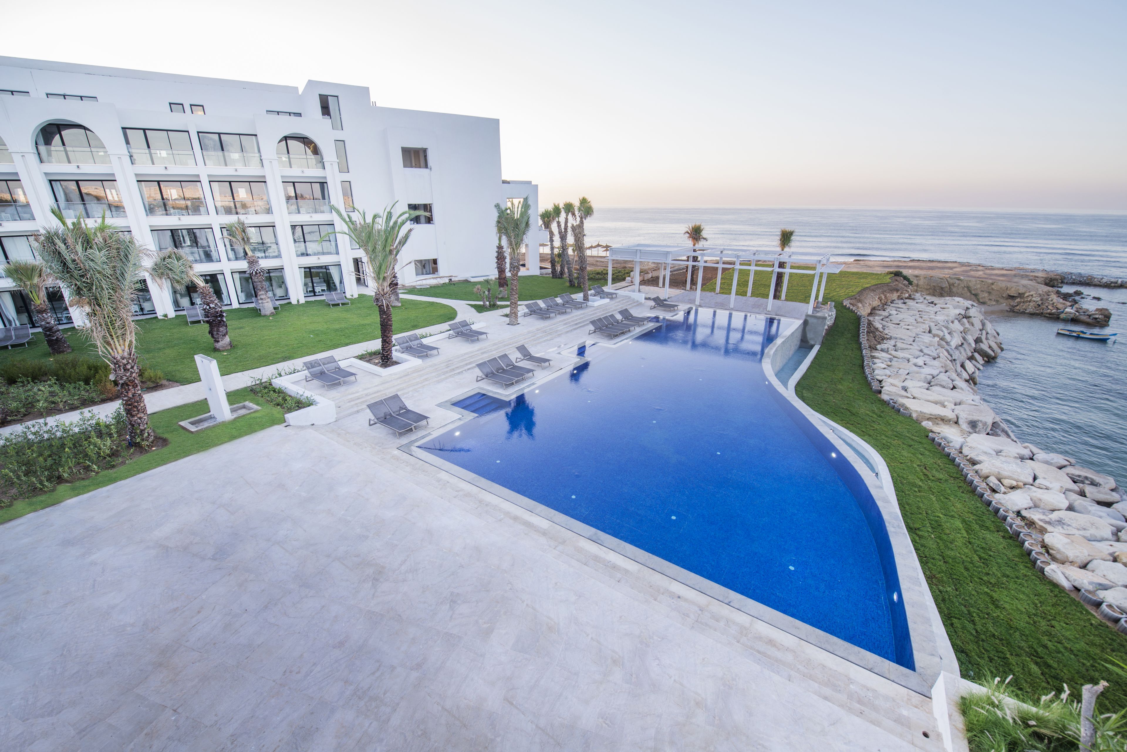 Un hôtel moderne doté d’une piscine, de chaises longues et offrant une vue sur l’océan.