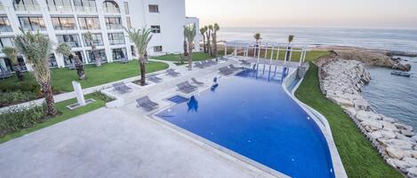 Un hôtel moderne doté d’une piscine, de chaises longues et offrant une vue sur l’océan.