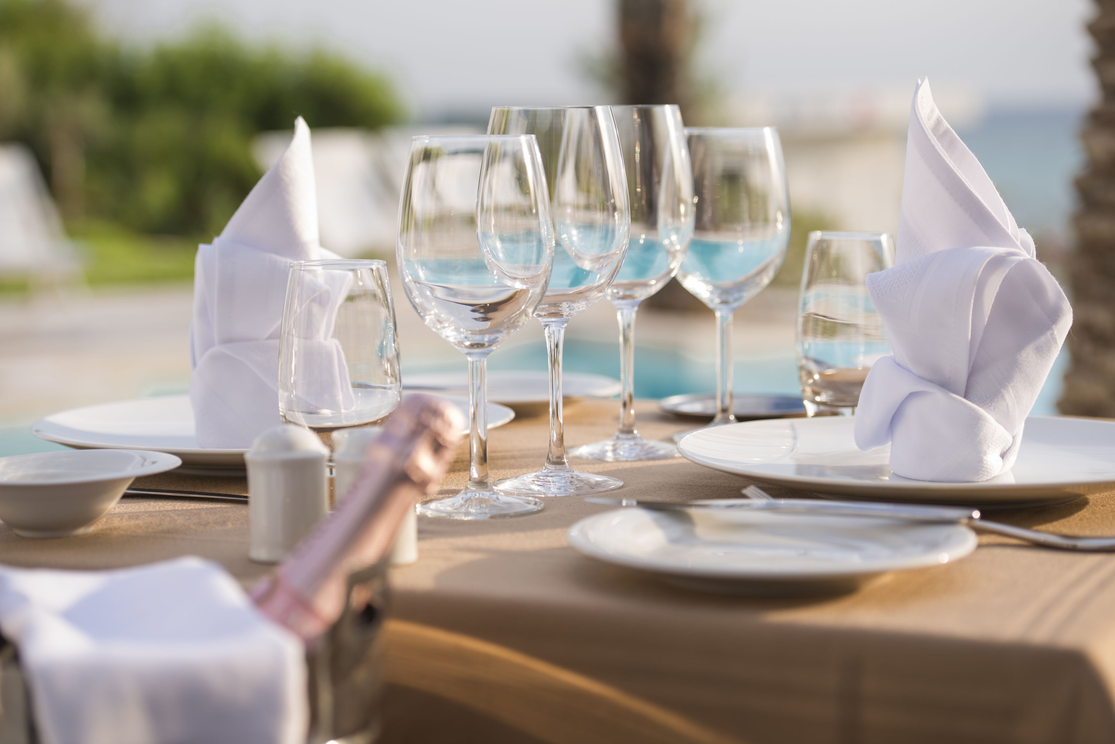 Una mesa lista para una comida, con cristalería transparente, servilletas blancas y vista al océano.