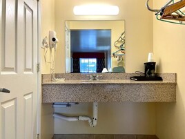 Un baño con encimera de granito, lavabo, espejo, secador de pelo y toallero.