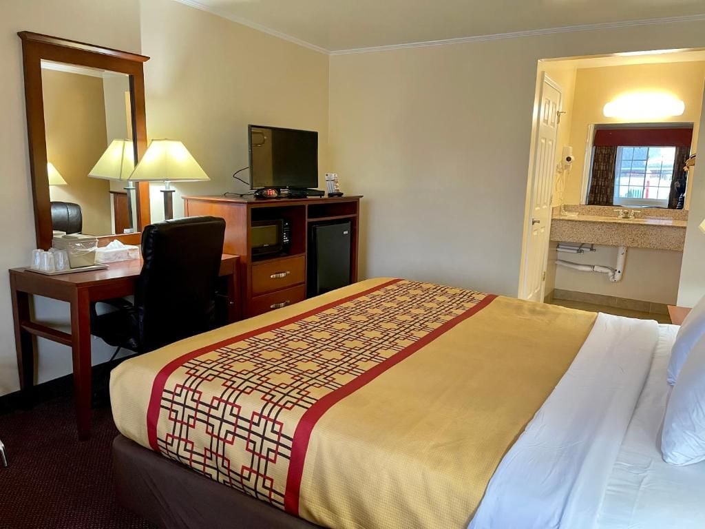 Una habitación de hotel con cama, escritorio con silla, televisor, microondas y refrigerador pequeño.