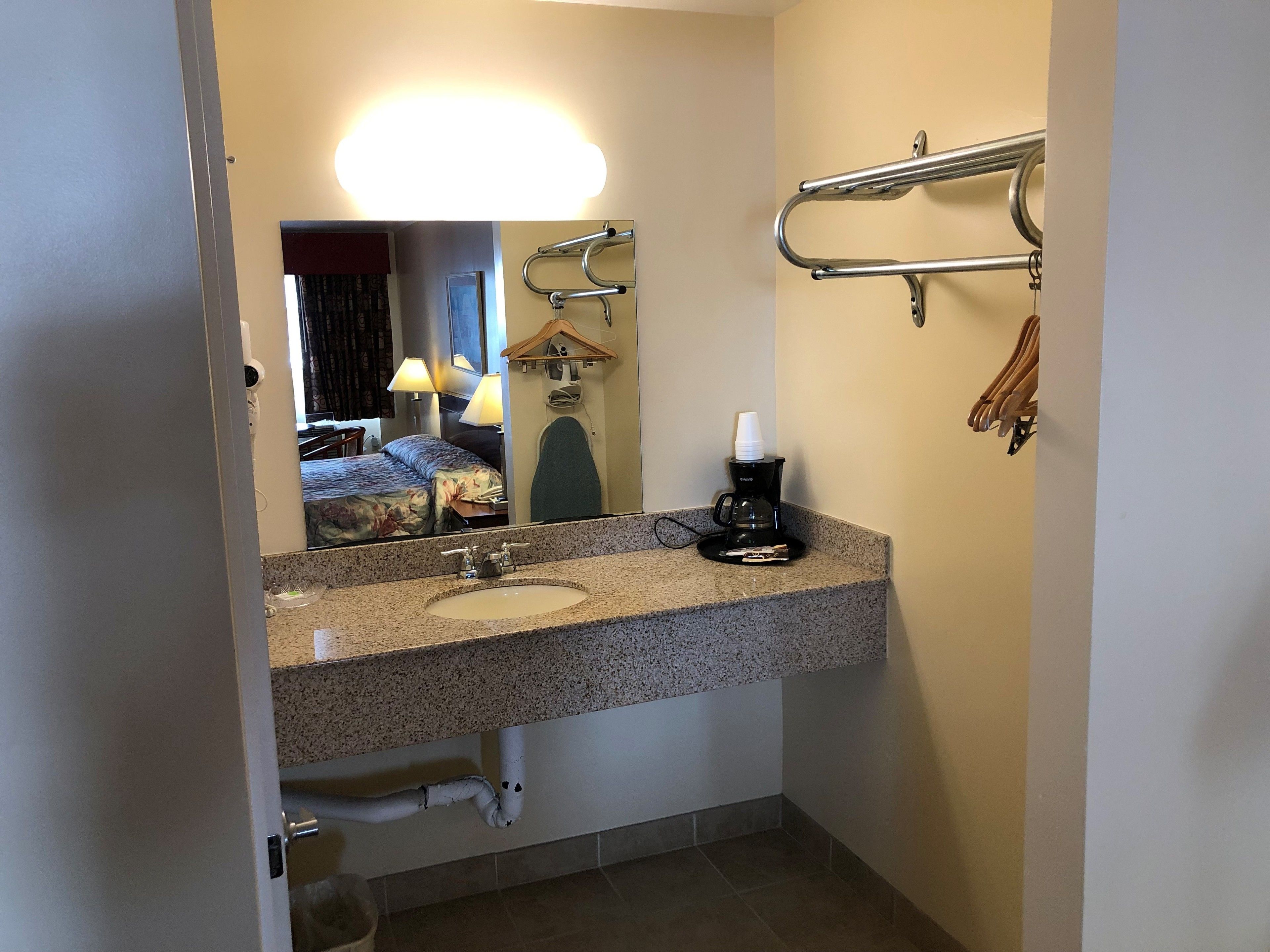 Un baño de hotel con lavamanos de encimera de granito, espejo, perchero y cafetera.