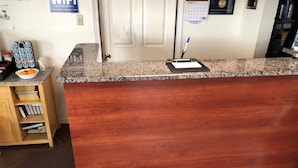 A reception desk with a wooden finish, a calendar on the wall, and a passport in a holder. - The Aventis Inn (Somers Point)
