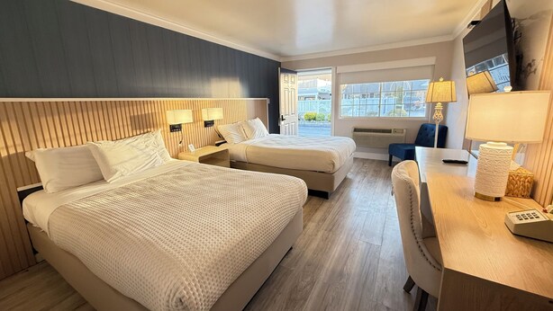 A hotel room with two beds, a desk, a chair, a TV, and a window with a view. - The Aventis Inn (Somers Point)