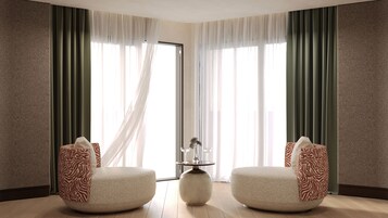 Una habitación con dos sillones, una mesita con un florero y copas de vino, y vistas a través de cortinas translúcidas.