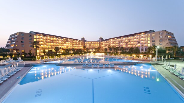 Un grand hôtel doté d’une piscine centrale, entourée de chaises longues et de parasols.