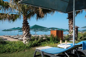 Ein Strandloungebereich mit Liegestühlen, Sonnenschirmen und Blick auf das Meer.
