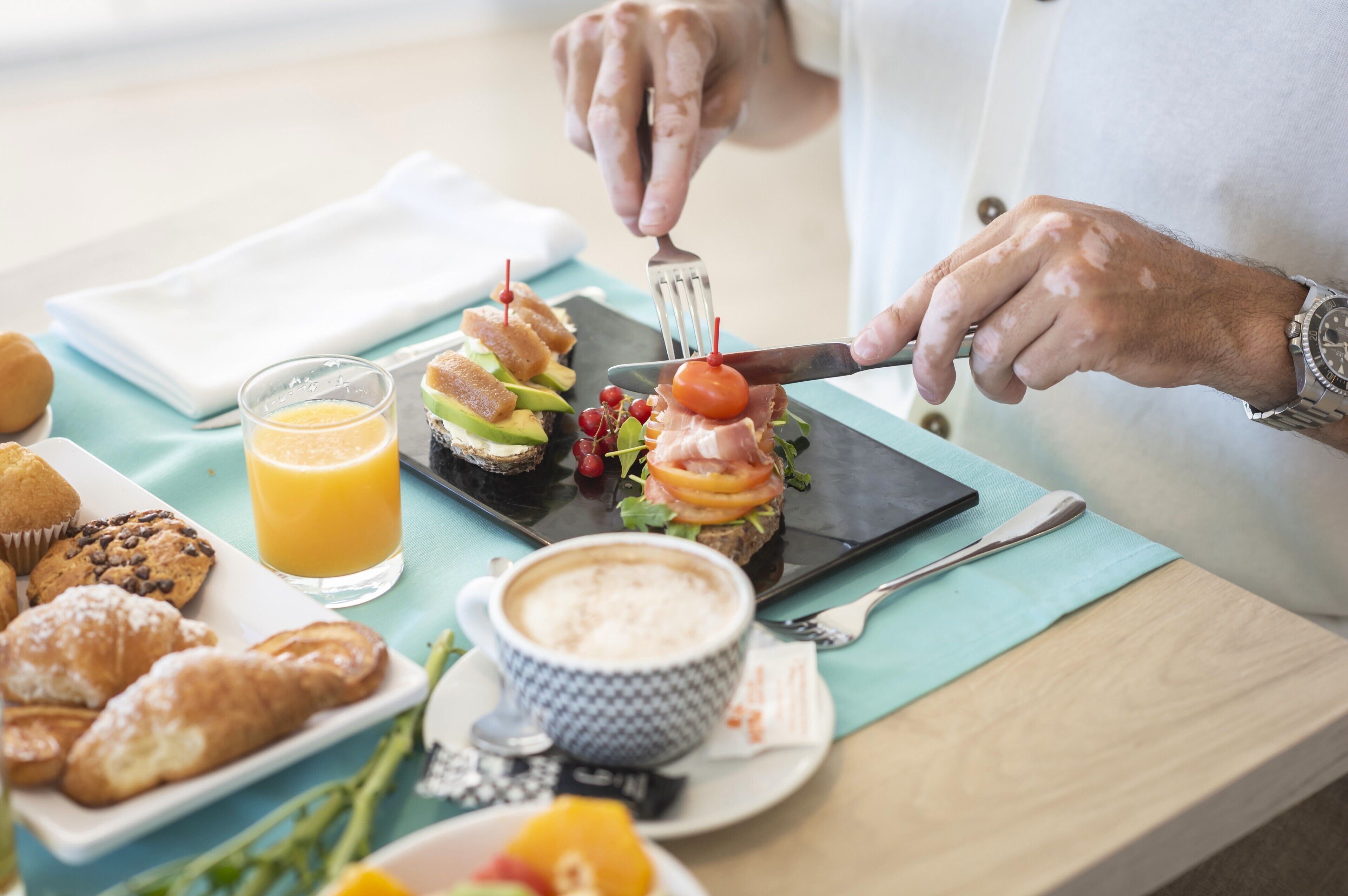 Une table dressée pour le petit-déjeuner avec des croissants, un verre de jus d’orange, une tasse de café et un sandwich, le tout présenté sur une tablette.