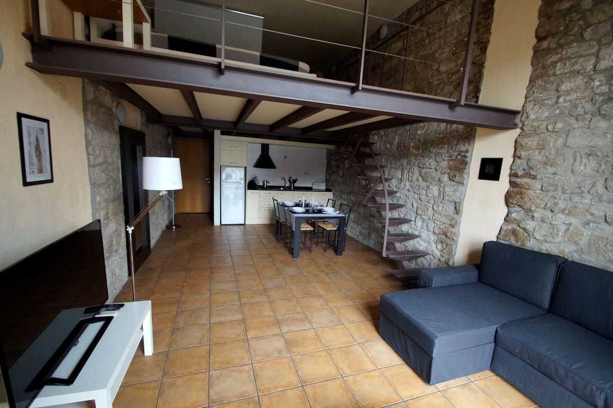 A spacious living area with a sofa, a dining table with chairs, and a kitchen in the background.