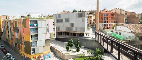 Un área urbana moderna con una combinación de edificios residenciales y comerciales, incluyendo un edificio de apartamentos de varios pisos con balcones y una gran chimenea industrial.