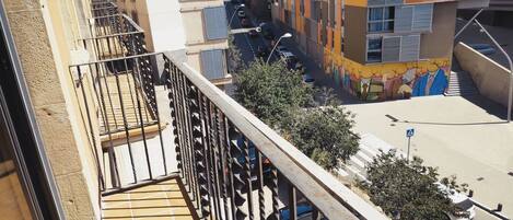 Una calle estrecha flanqueada por edificios, con un paso de peatones y una escalera que conduce a un balcón.